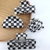 A collection of black and white checkered rectangle hair claw clips arranged on a wooden surface.