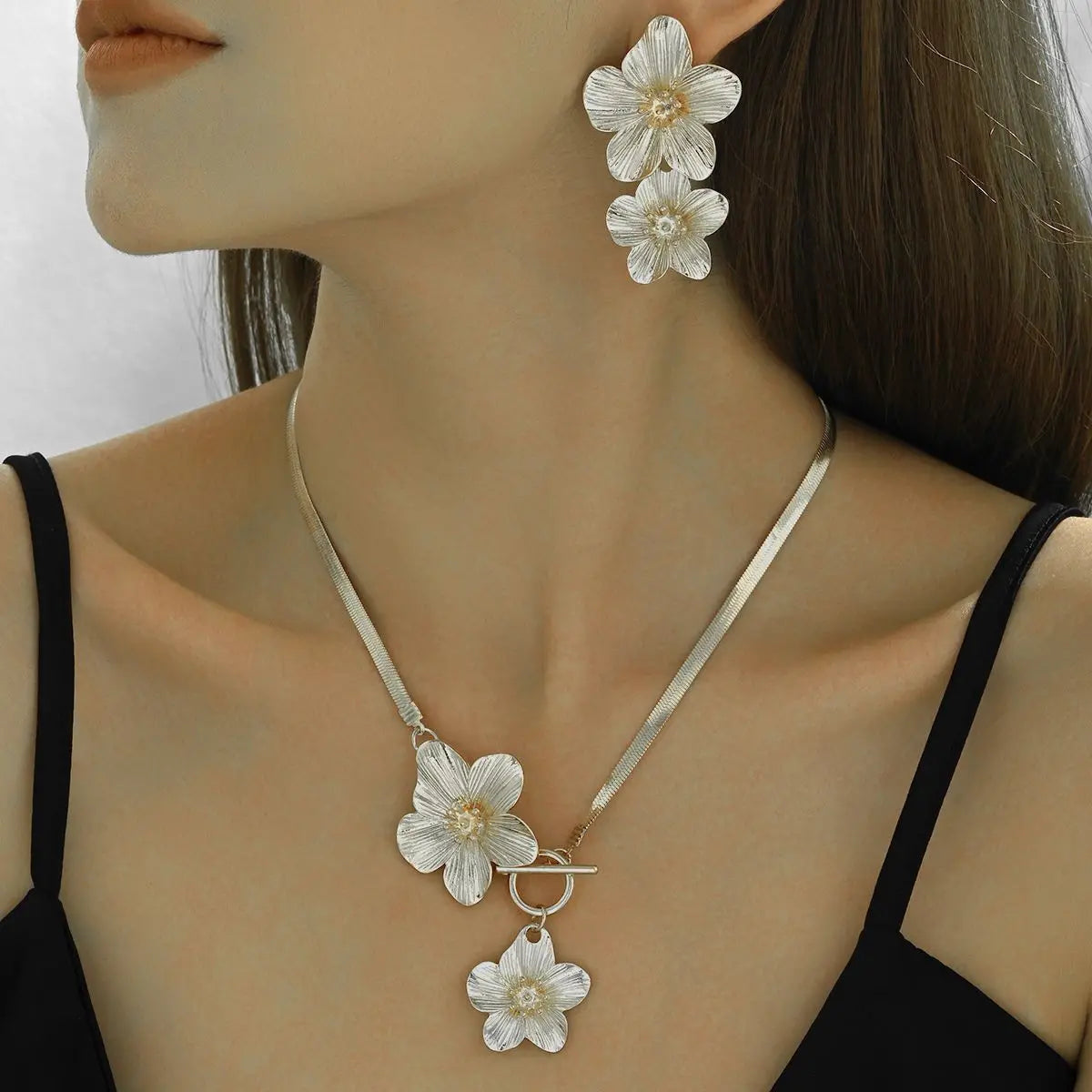 A close-up of a woman wearing a silver floral pendant necklace and matching earrings against her neck and hair.