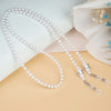 Two strands of white pearl beaded eyewear chains displayed on a beige surface with soft lighting.