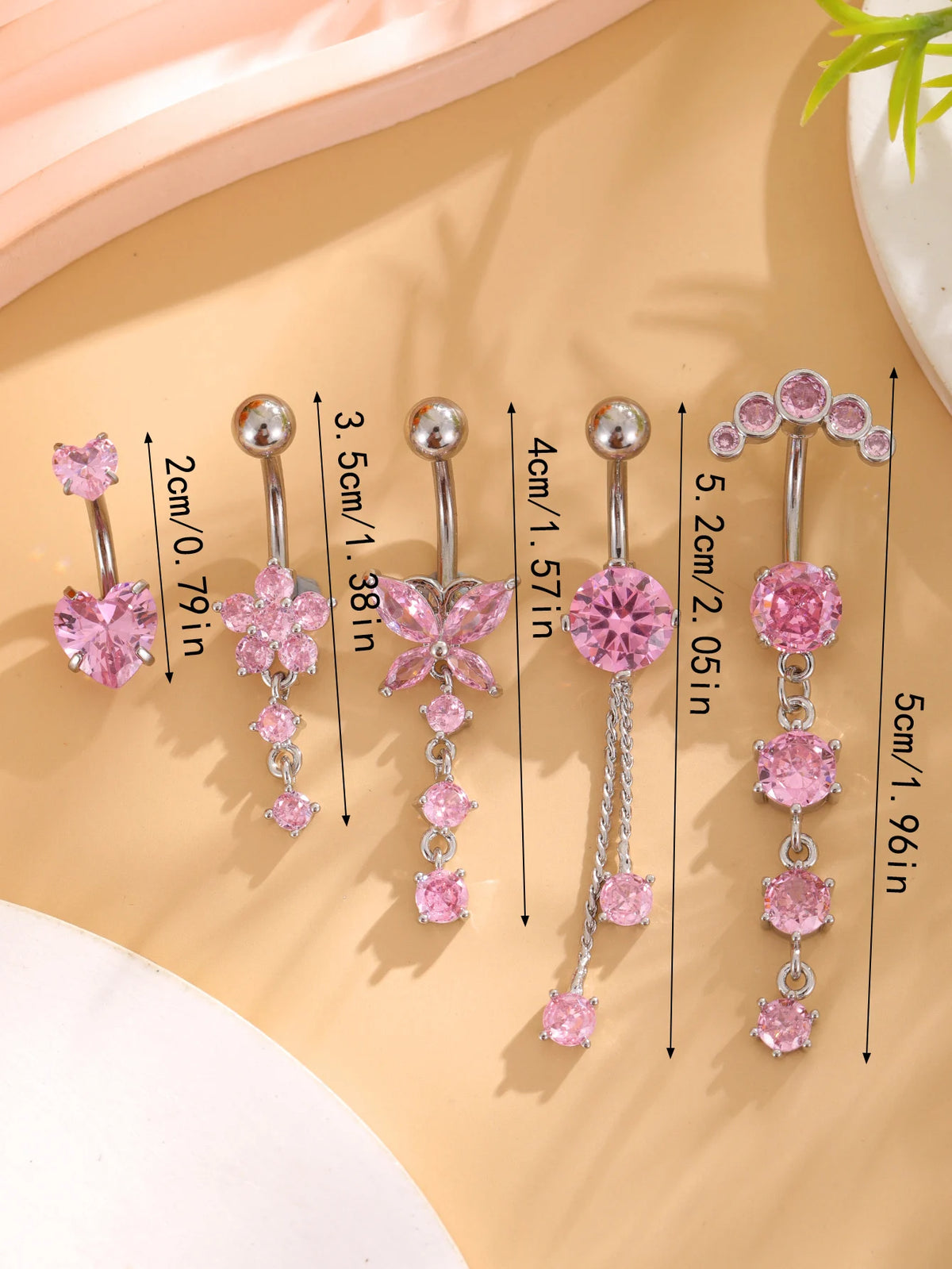 A set of five gold stainless steel dangled belly button rings featuring pink gemstones and various lengths.
