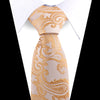 A close-up of an elegant men's floral paisley silk necktie in beige with gold embroidery, shown against a white shirt.