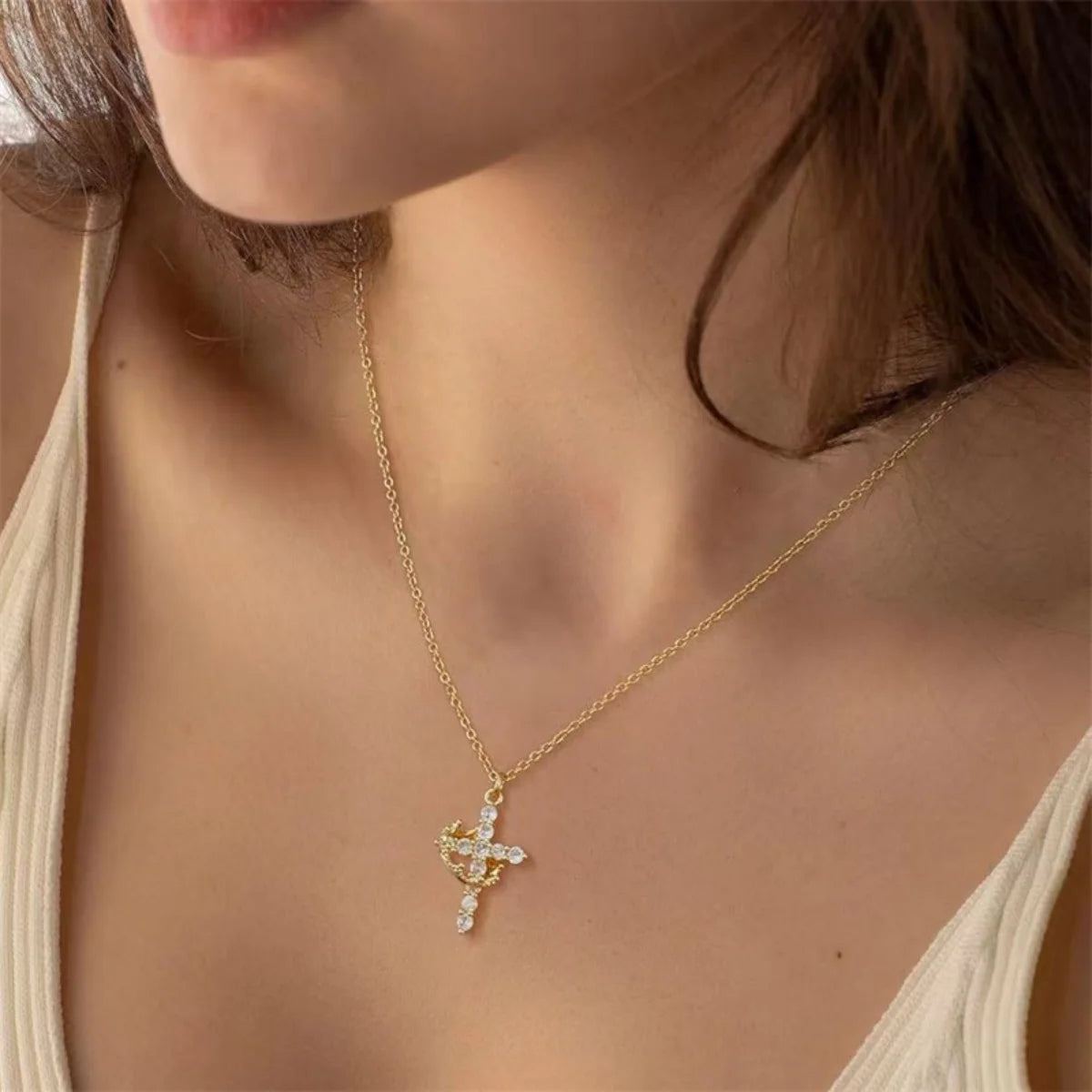 A close-up of a gold-toned cross pendant necklace worn around the neck against light skin.