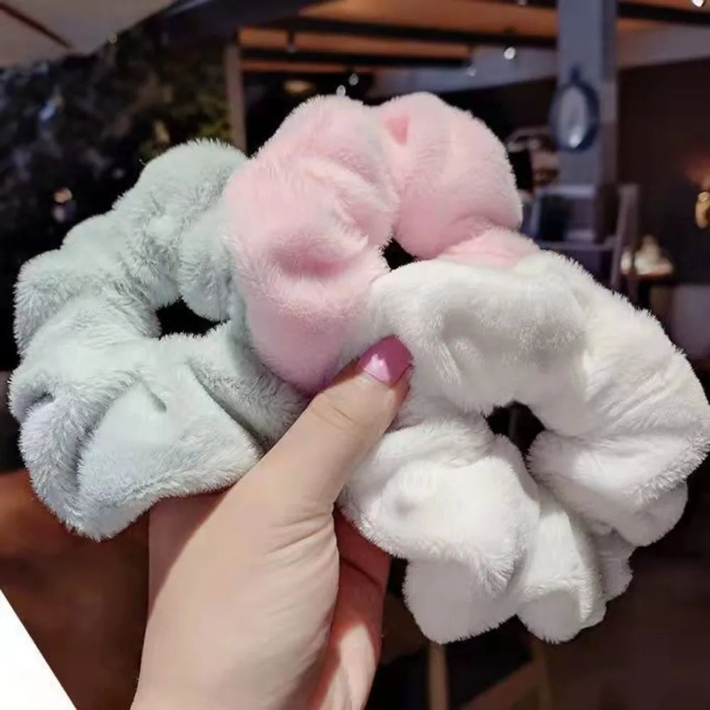 Une main tient un ensemble de élastiques pour cheveux en tricot doux dans des couleurs rose pastel et blanc.