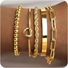 A collection of four chunky gold-tone bangles and a gold-tone hoop earring displayed on a brown surface.