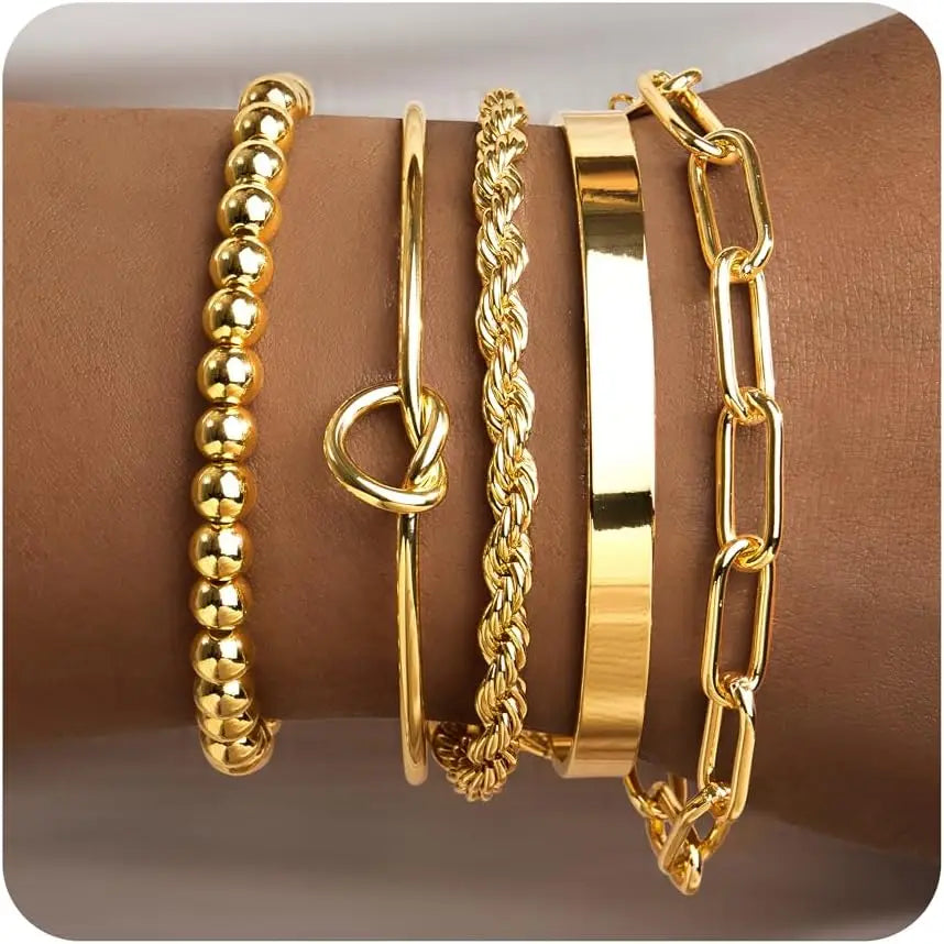 A collection of four chunky gold-tone bangles and a gold-tone hoop earring displayed on a brown surface.