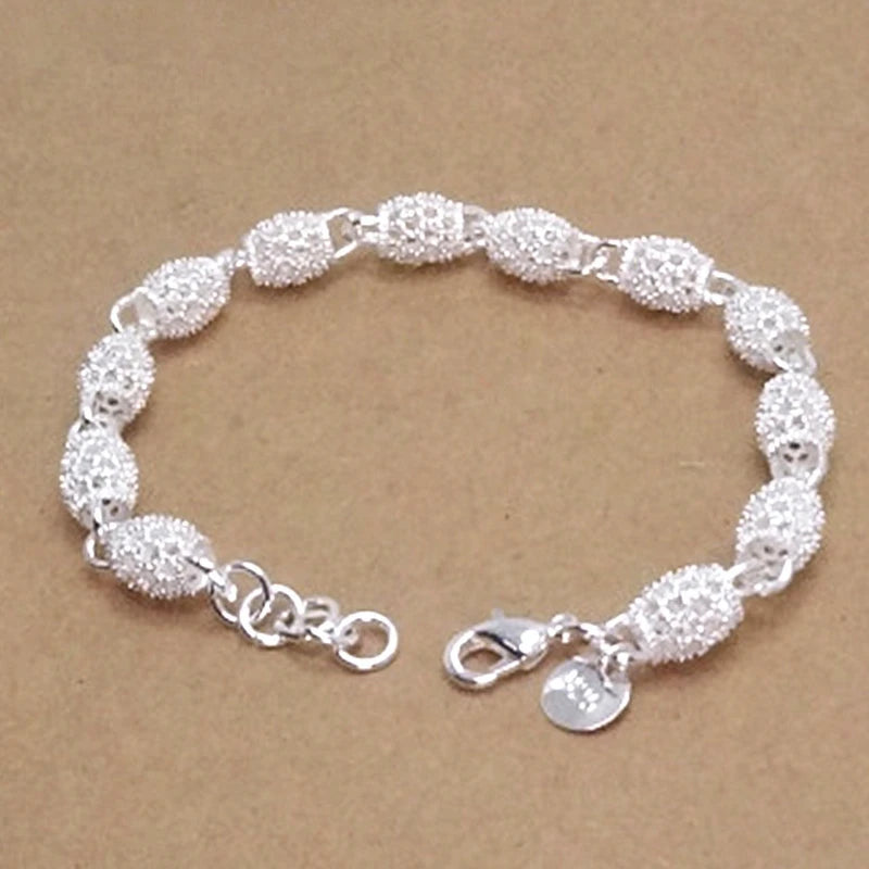 A bracelet of small, textured silver bangles and a charm on a brown background.