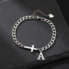 A silver stainless steel Cuban chain bracelet with a cross and the letter A charm resting on a black surface.