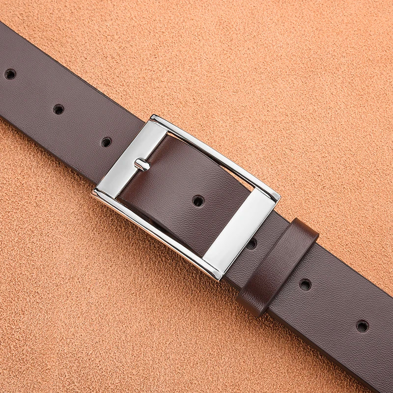 A close-up of a dark brown PU leather belt with a silver metal pin buckle lying diagonally on a light orange background.