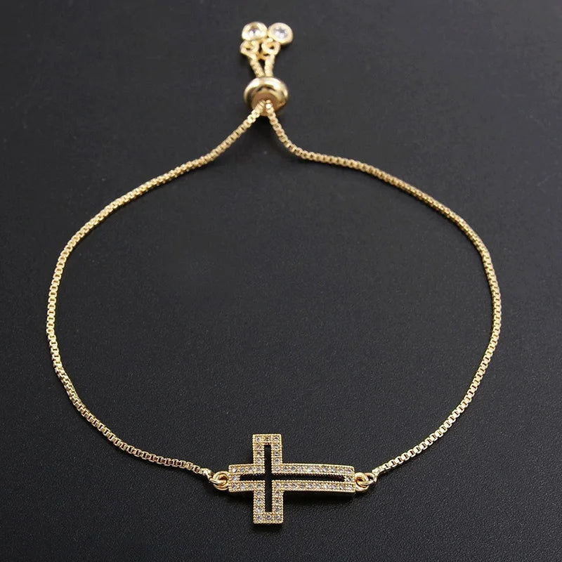 A gold-plated cross bracelet with cubic zirconia stones is displayed against a dark background.