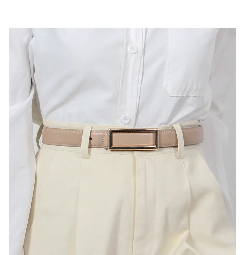 A beige faux leather belt with a gold buckle worn over a white collared shirt and light cream trousers.