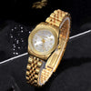 A gold-toned quartz wristwatch with a white face and rhinestone accents on a black background.