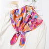 A vibrant silk scarf featuring floral patterns in shades of orange, pink, and purple tied around a white shirt.