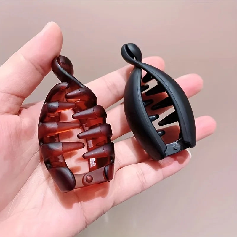 Una mano sostiene una pinza de plátano negra y una pinza para el cabello marrón anaranjado contra un fondo claro.