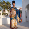 Une femme modélise une écharpe florale bleu et or avec des motifs complexes dans un cadre architectural extérieur.