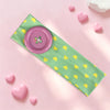 A pink and lime green fabric headband with a round button and yellow polka dots, lying on a pink surface.
