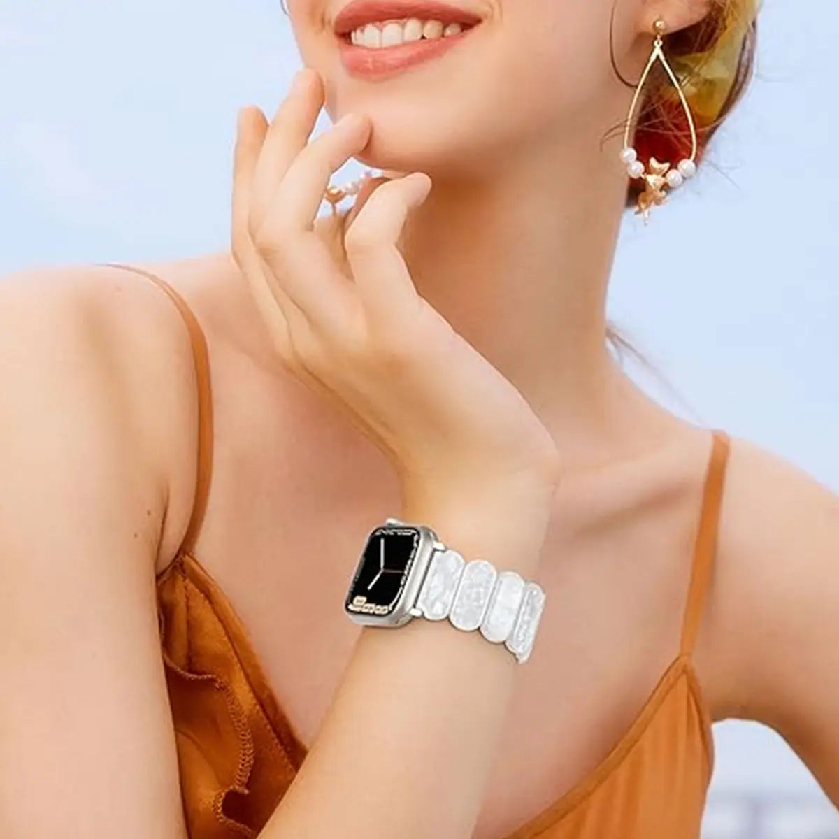 Une femme portant une montre argentée à bracelet texturé, sur fond de ciel lumineux.
