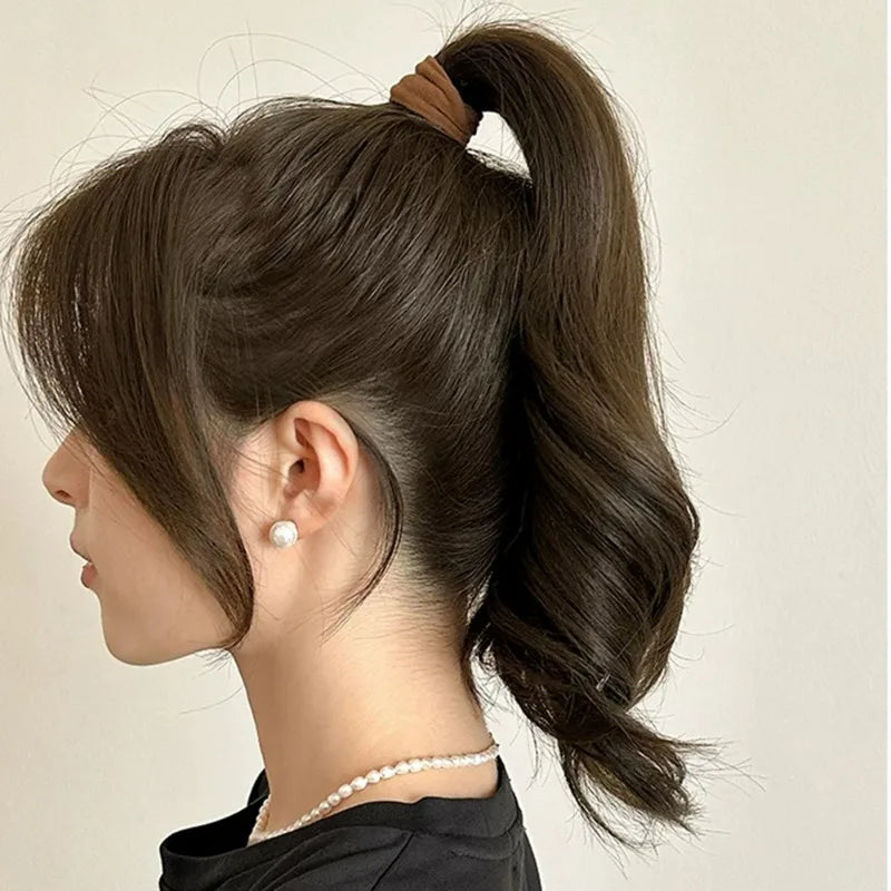 A side profile of a woman with dark brown hair styled in a high ponytail secured by an extra-wide elastic band and a pearl ne