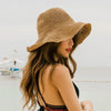 A woman wearing a hand-woven straw visor hat while standing near the water.