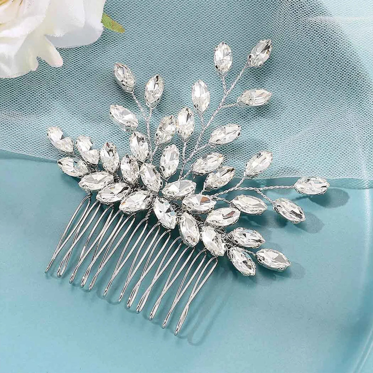 Peigne pour cheveux de mariée en cristal argenté, présenté sur une surface bleu clair.
