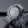 A silver stainless steel watch with a black dial and bezel is displayed on a dark surface.