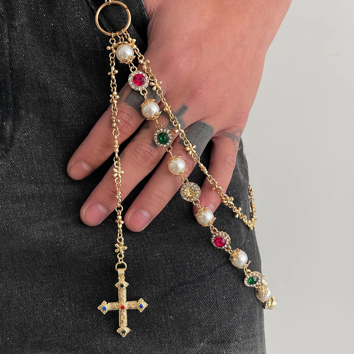 A gold chain necklace featuring pearl and gemstone beads, ending in a cross pendant, being held by a person.