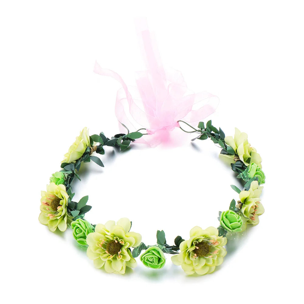 A green floral wreath headband with pink sheer ribbon, featuring small roses and leaves.