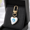 Gold heart-shaped keychain with a white and blue evil eye design displayed in a black velvet box.