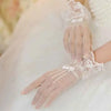 A close-up of sheer lace fishnet evening gloves worn by a person in a white dress.