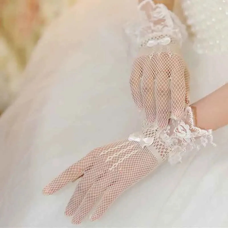 A close-up of sheer lace fishnet evening gloves worn by a person in a white dress.