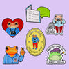 A set of enamel brooches featuring frogs and a green speech bubble with text about sleeping in three hours.