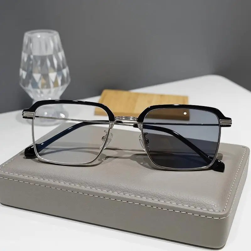 A pair of black-framed photochromic anti-blue light reading glasses resting on a gray leather case.