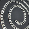 A silver geometric face chain necklace coiled on a dark background.