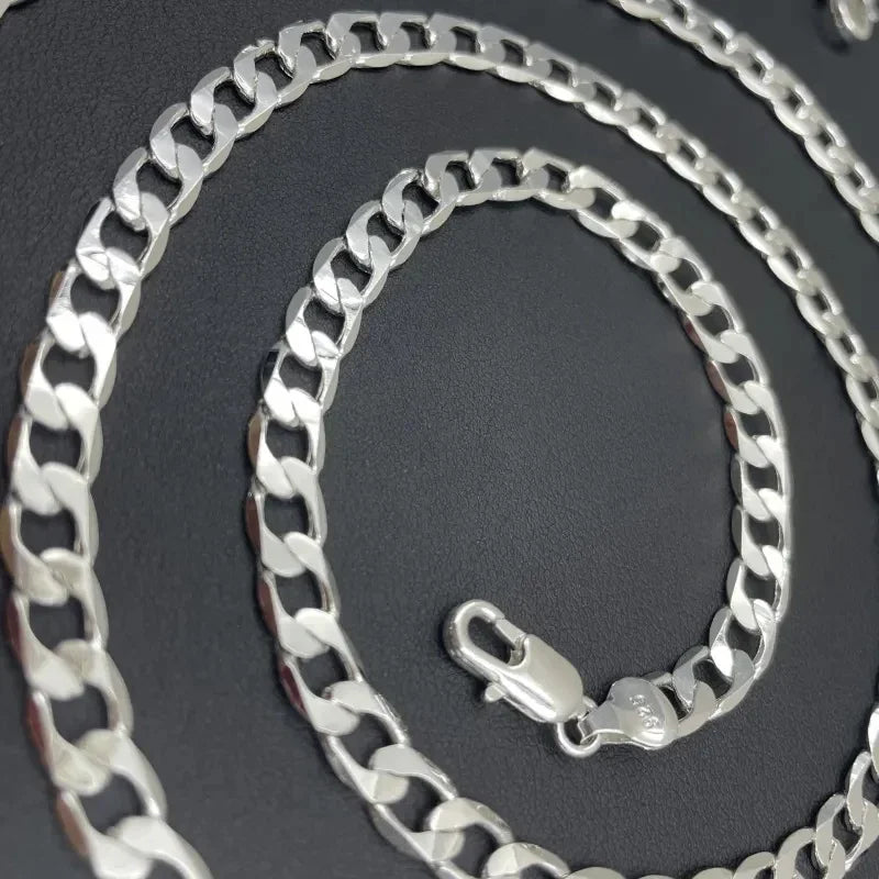 A silver geometric face chain necklace coiled on a dark background.