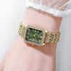 A gold-toned rhinestone quartz wristwatch with a green face and gold band worn on a wrist.