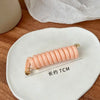 A light peach rubber braided ponytail holder measuring 7cm resting on a white ceramic plate.
