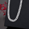 Un collier chaîne argenté est exposé sur une surface noire à côté de feuillage rouge.