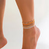 A close-up of a woman's ankle wearing multiple strands of colorful seed bead anklet bracelets.