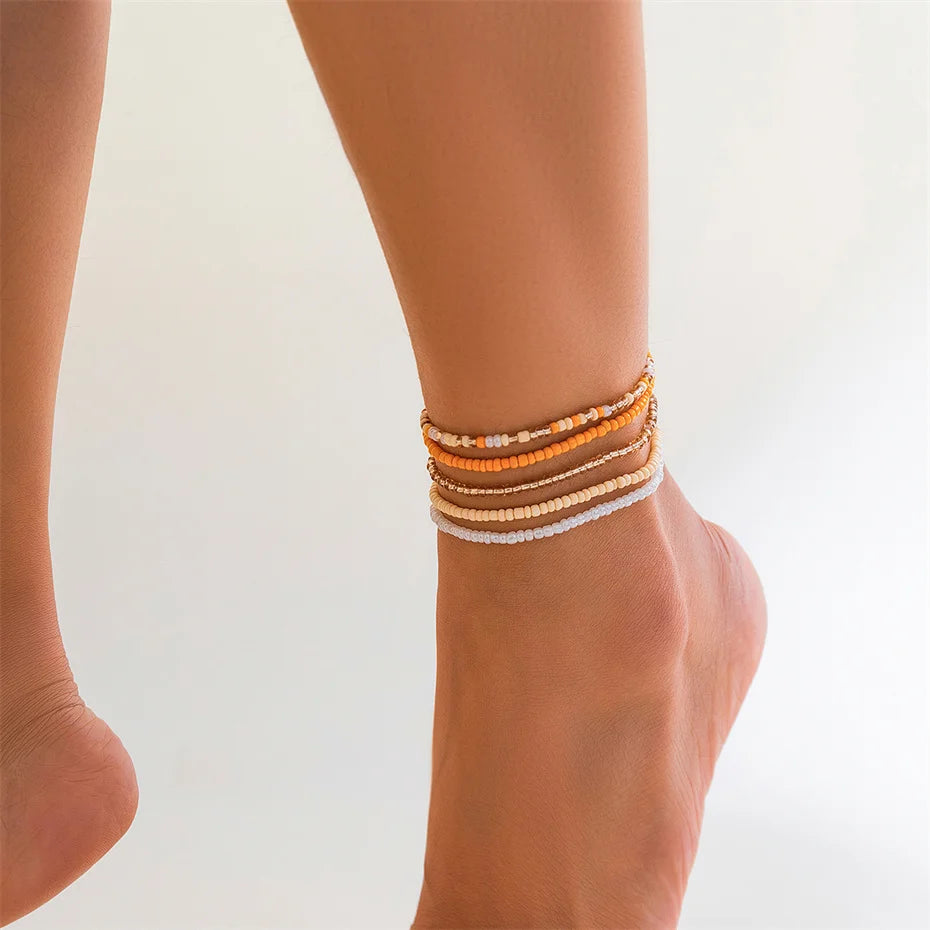 A close-up of a woman's ankle wearing multiple strands of colorful seed bead anklet bracelets.