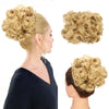 A woman shows off a blonde synthetic curly chignon hairstyle, featuring voluminous curls and a messy bun look.