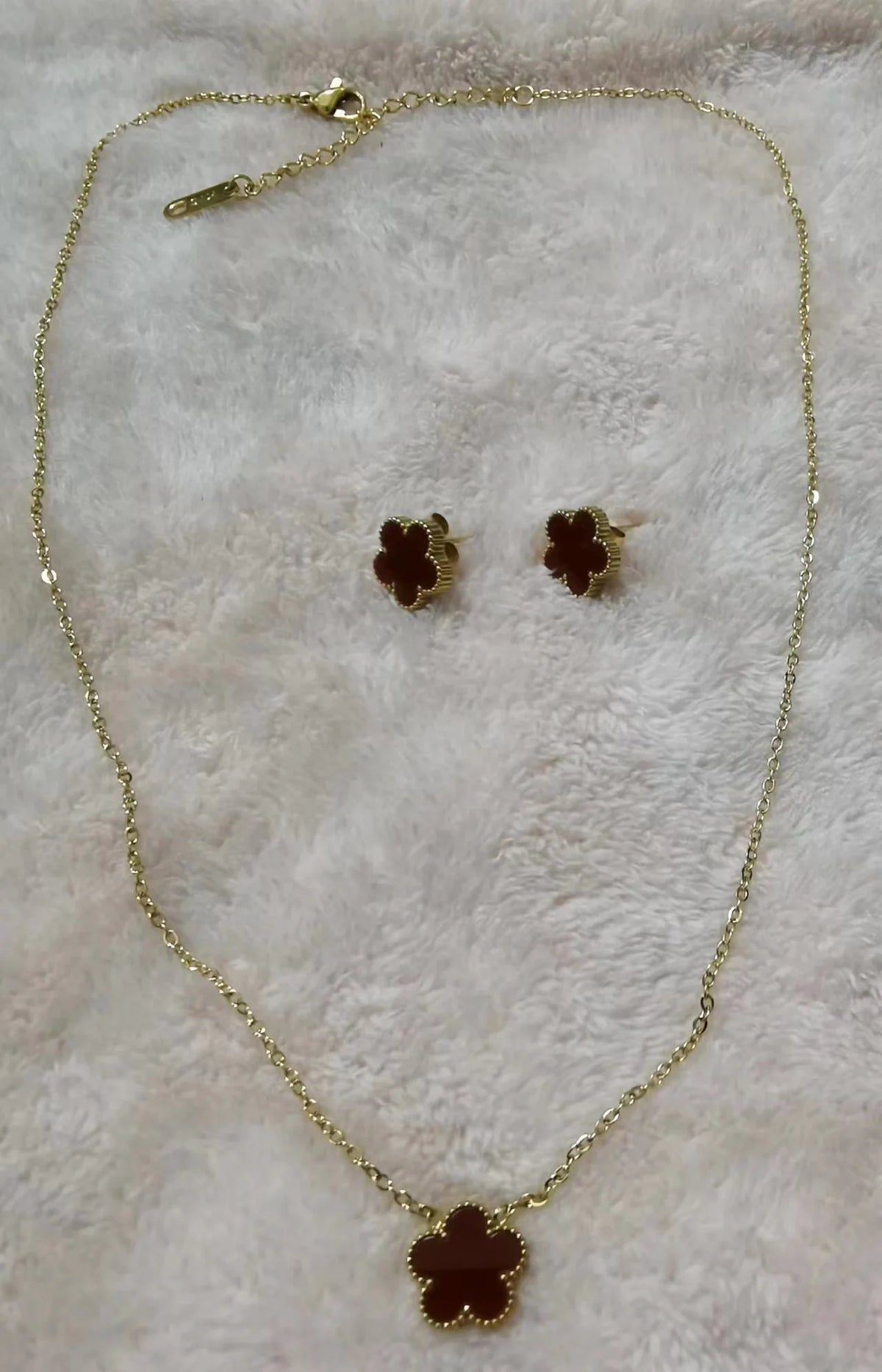 Collar de planta de acero inoxidable chapado en oro con pendientes a juego, exhibido sobre un fondo peludo