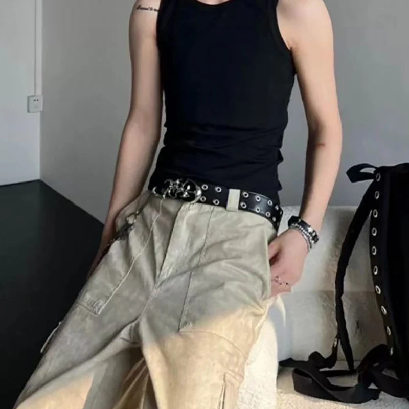 A person wearing a black tank top and light beige pants with a silver belt and bracelet.