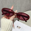 A hand holds a pair of maroon cat eye sunglasses against a light background.