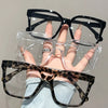 Una mano sostiene unas gafas cuadradas transparentes con montura negra y un par de gafas de estampado de leopardo.