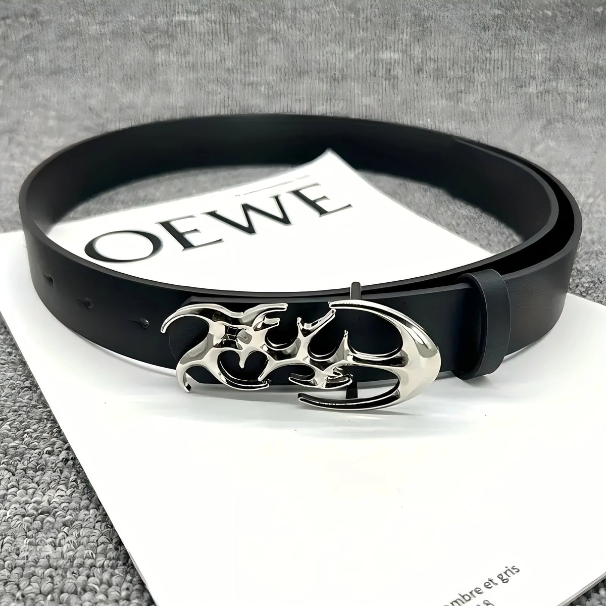 Black fashion belt with a silver skull buckle resting on a white card.