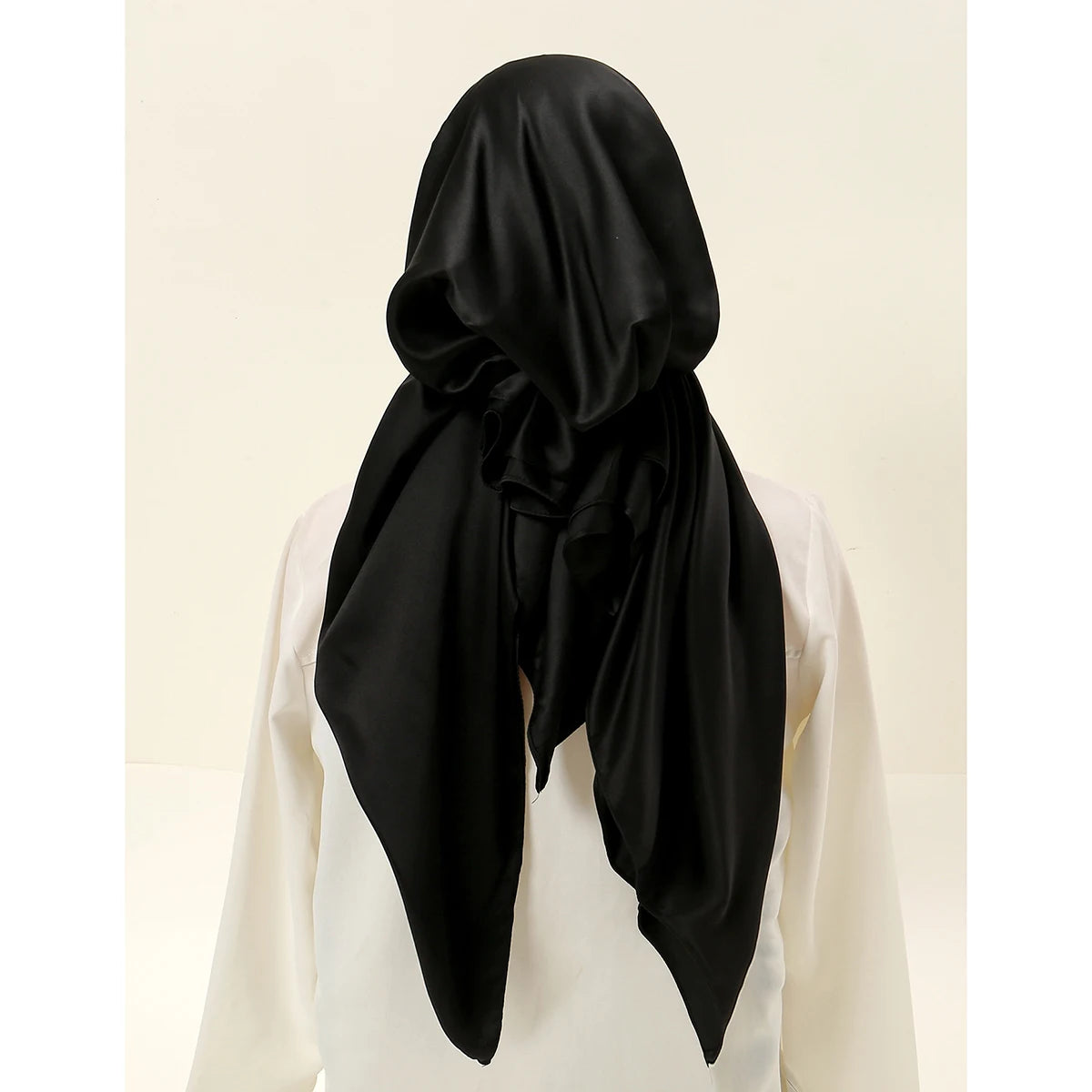 A black satin silk hijab is draped and styled on a white garment.