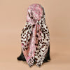 A pink and white leopard print square satin scarf tied in a flowing drape.