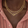 Gold layered Cuban link necklace worn around the neck against a pink knitted sweater.