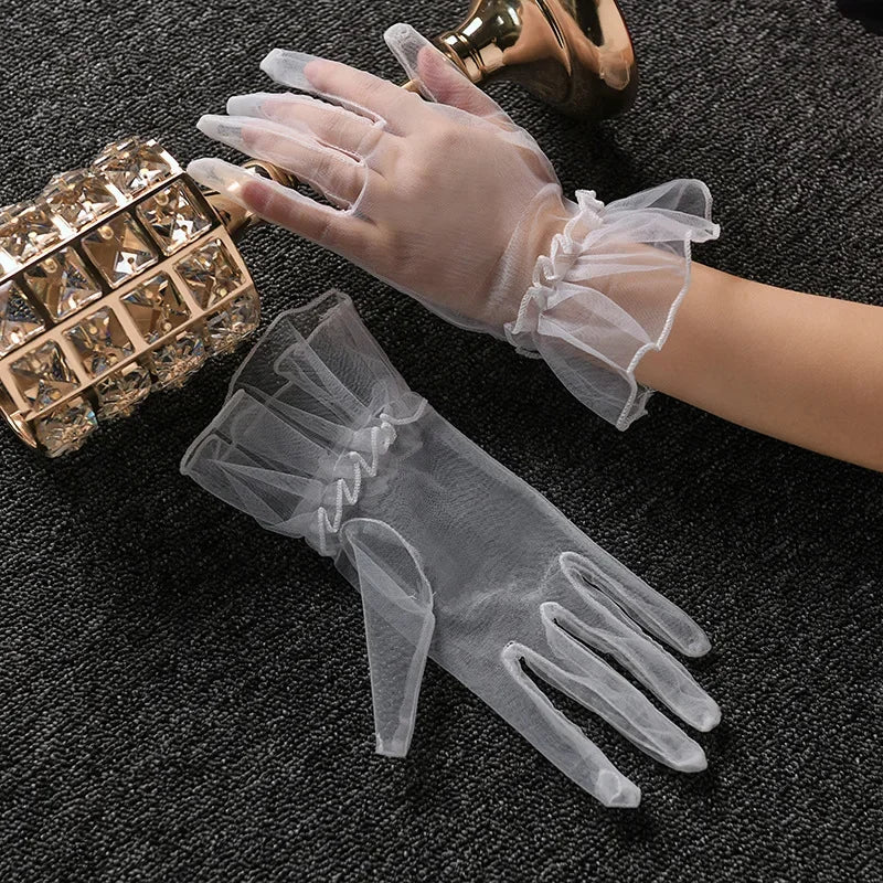 A hand wearing sheer white lace tulle finger gloves is shown next to a gold-toned accessory.