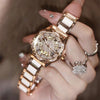 Una mano sostiene un reloj de pulsera de diamante de cuarzo dorado con correa blanca y un dije cristalino brillante.