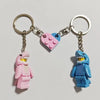 A keychain set featuring two shark-themed building block charms, one pink and one blue, attached to silver split rings.